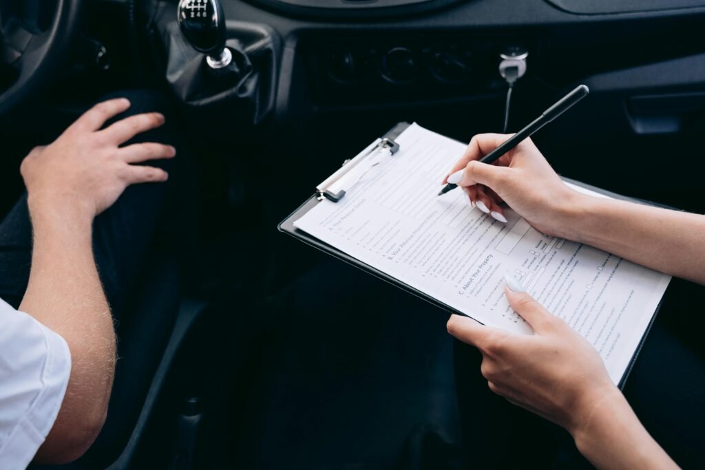 pexels-photo-8943323-8943323 Close-up of a person writing on a clipboard inside a car, showing hands and a gear shift.